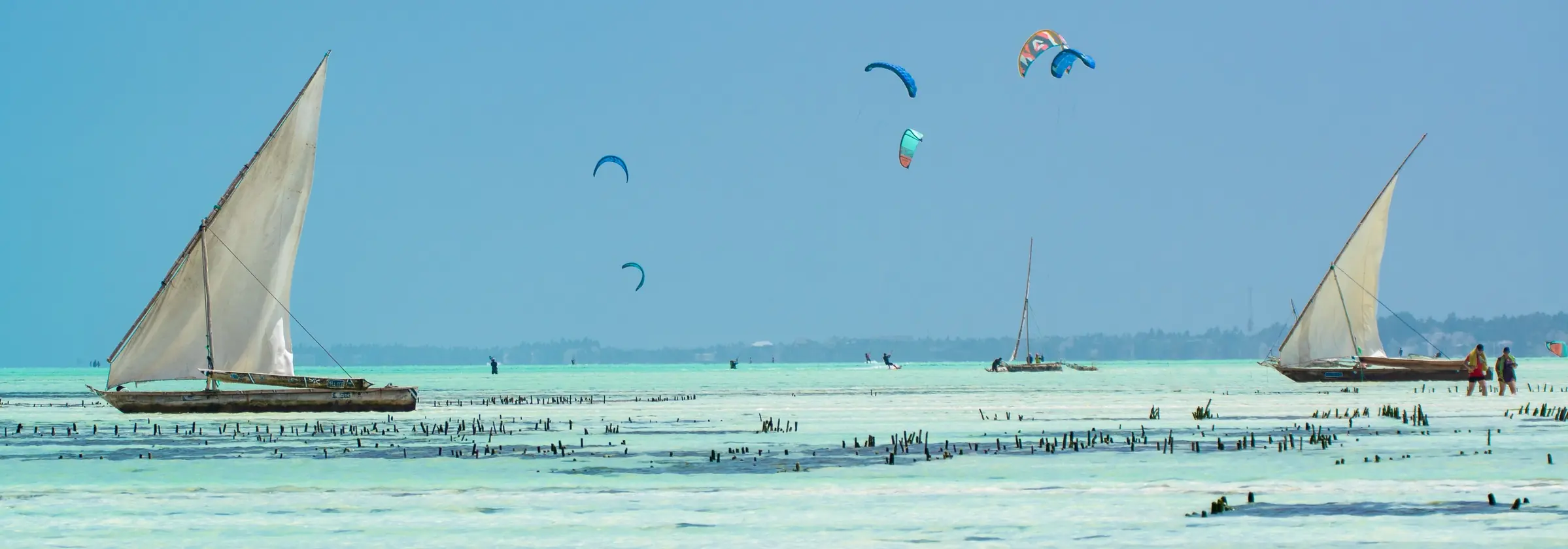 Two dhows and four kites over the Jambiani lagoon at low tide, with seaweed farms in the shallow water
